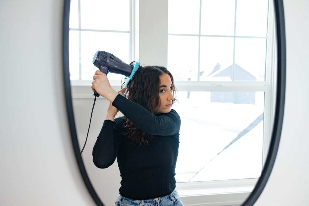 young woman using the clm volumizer in front of a mirror